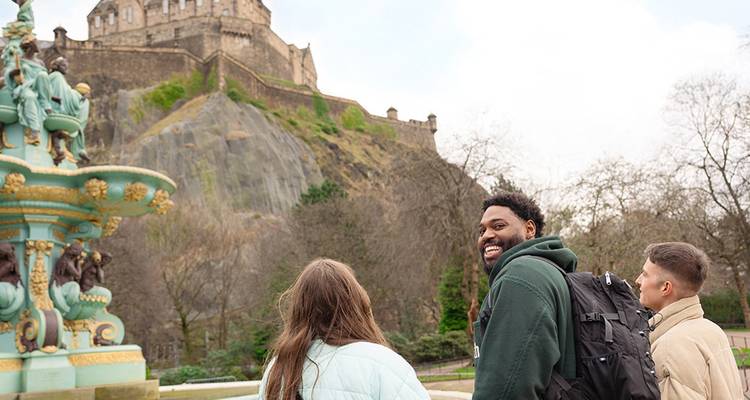 Reizigers kijken omhoog naar Edinburgh Castle dat op een rotsachtige heuvel staat naast een decoratieve fontein