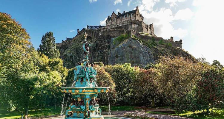 Vue panoramique d'un château sur une colline avec une fontaine colorée au premier plan.