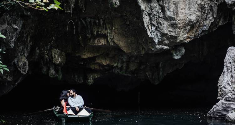 Un couple romantique dans une petite barque dérive vers l'entrée spectaculaire d'une grotte calcaire.