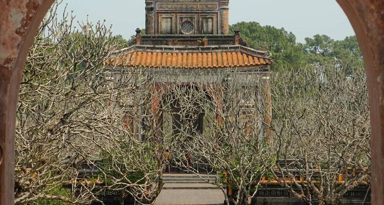 Vue encadrée à travers une arche d'un pavillon de tombeau royal orné entouré d'arbres dénudés.