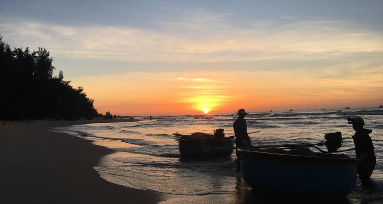 Pêcheurs en silhouette avec des coracles rondes sur une plage tropicale pendant un coucher de soleil éclatant.