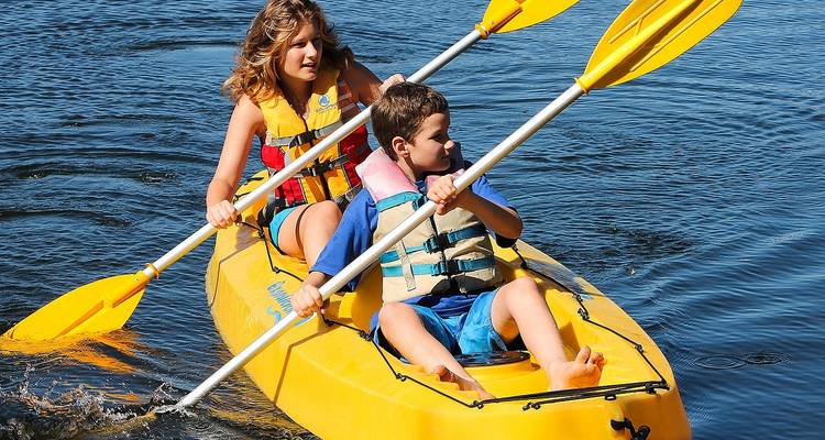 Deux enfants pagaient ensemble dans un kayak jaune vif sur une eau bleue calme.