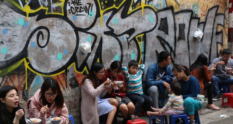 Les habitants mangent de la nourriture de rue sur de minuscules tabourets le long d'une ruelle couverte de graffitis.
