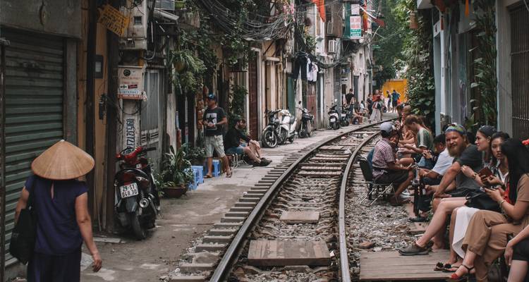 Des touristes sont assis à côté des voies ferrées actives bordées de bâtiments étroits et de cafés dans la célèbre rue du train de Hanoï.