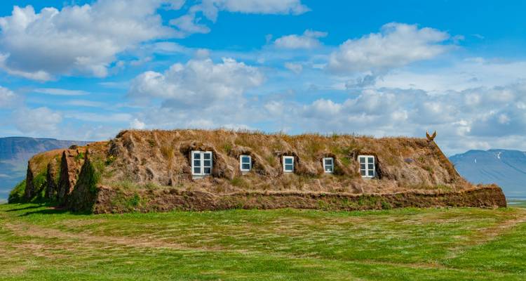 Traditioneel IJslands plaggenboerenhuis met grasbegroeid dak onder een heldere blauwe hemel