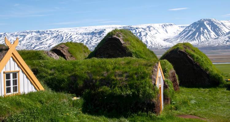 Cluster van boerenhutjes met grasendaken tegen de achtergrond van besneeuwde bergen onder een heldere hemel