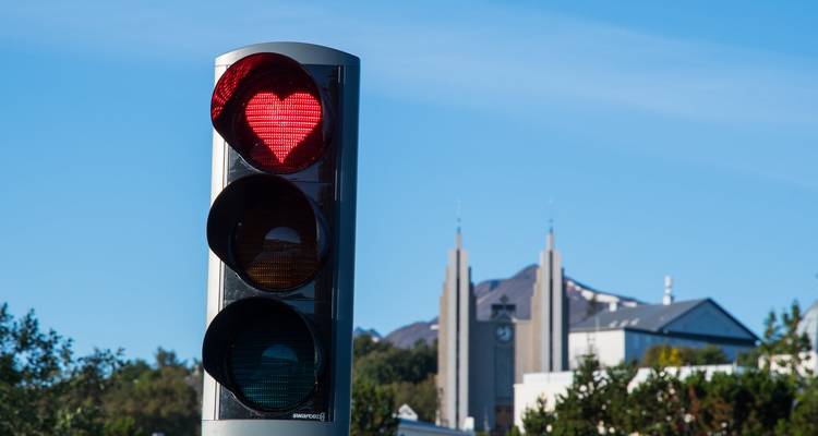 Verkeerslicht met een rood hartvormig signaal tegen een blauwe lucht en verre kerktorens