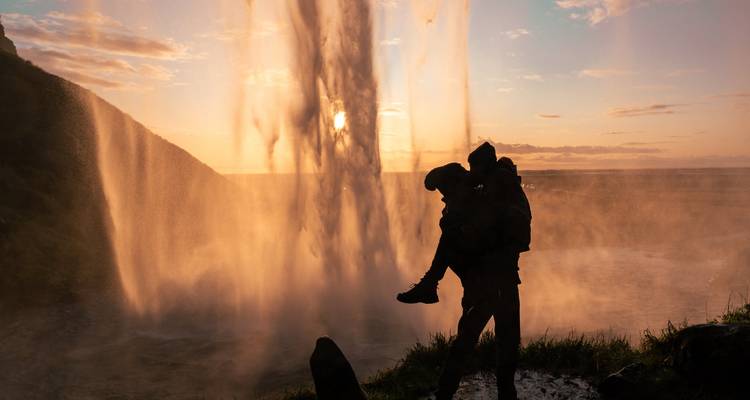 Silhouette of a couple in front of a waterfall during sunset.