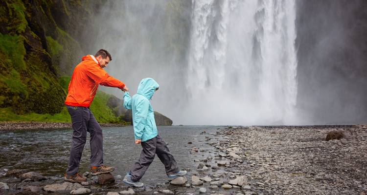 Father and child walking on the rocks near a waterfall.
