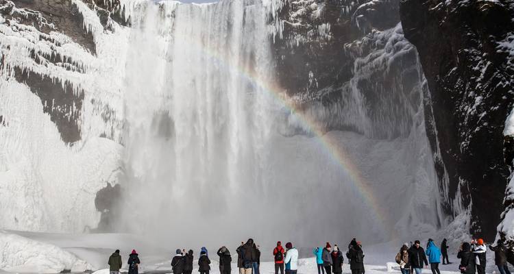People gathered in front of a snowy waterfall with a rainbow.