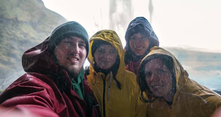 Group selfie taken under a waterfall with water droplets visible.