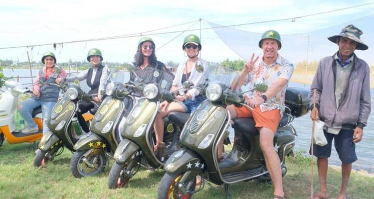Groupe de personnes sur des scooters au bord d'un lac avec un ciel dégagé.
