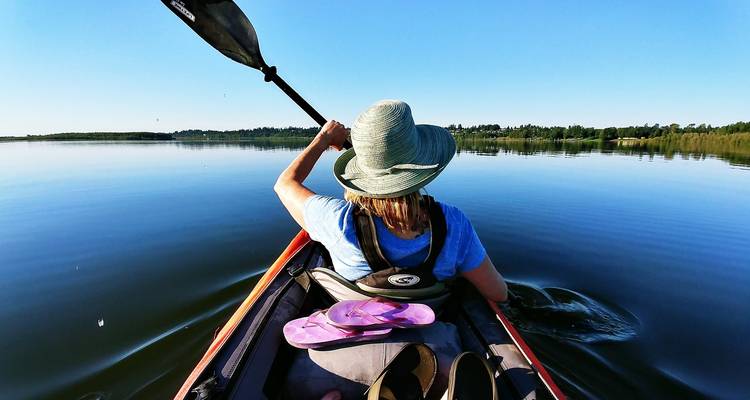 Vue à la première personne depuis un kayak fendant une eau bleue immobile par une journée ensoleillée.