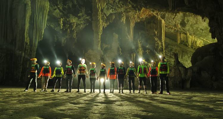 Des aventuriers casqués se tiennent alignés à l'intérieur d'une vaste chambre de grotte illuminée, leurs lampes frontales brillant.