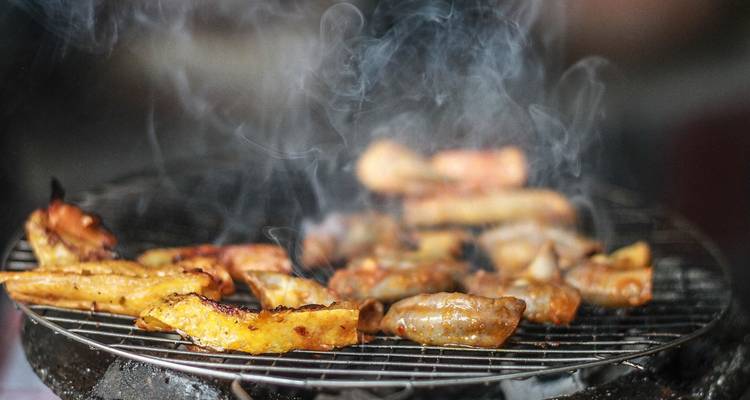 Des viandes assorties grésillent sur un grill au charbon de bois avec de la fumée qui tourbillonne vers le haut.