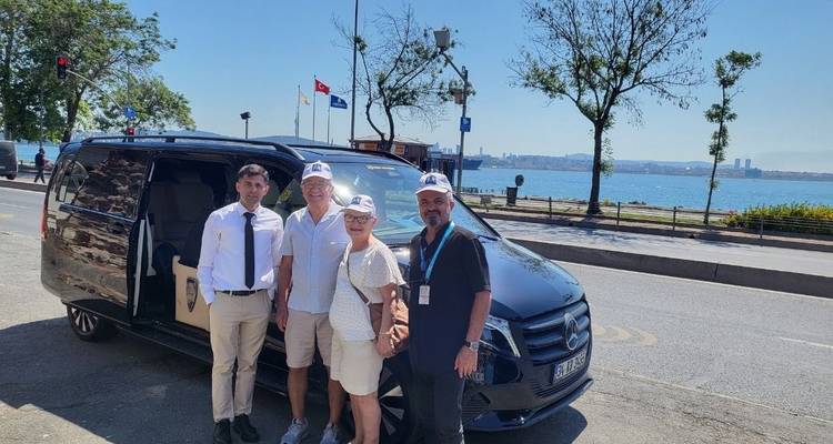 Groep mensen die poseren voor een zwarte bestelwagen bij een kustweg.