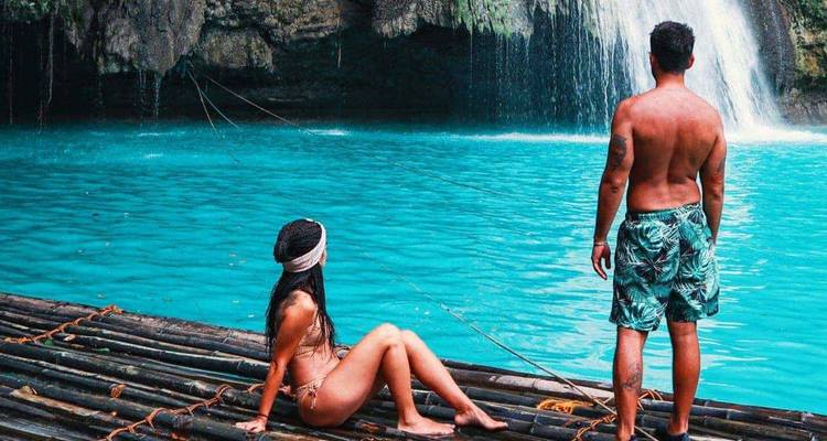 Un couple se détend sur un radeau en bambou face aux chutes de Kawasan turquoise sous des falaises luxuriantes.