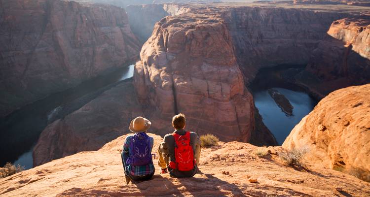 Deux personnes assises au bord de Horseshoe Bend, surplombant la rivière.