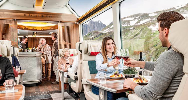 People enjoying a meal inside a train with a scenic mountain view from windows.