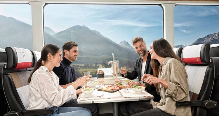 Group of people dining inside a train with mountain views through large windows.