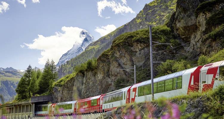 A red train moves through rocky cliffs with the Matterhorn in the background.