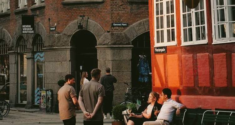 Vrienden genieten van drankjes buiten een rood geschilderd Kopenhagse gebouw tijdens het gouden uur