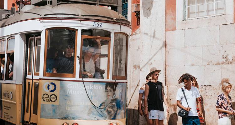 Vintage gelbe Straßenbahn fährt an Fußgängern vorbei auf einer sonnenbeschienenen Lissabonner Straße mit historischen Fliesen.