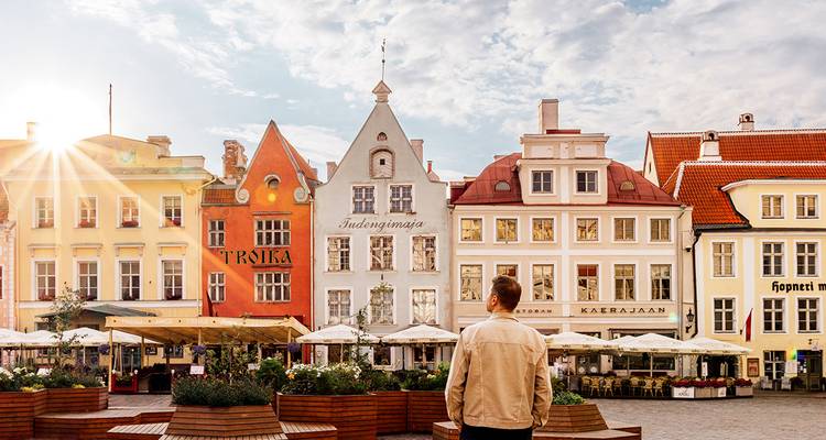 Traveler admiring colourful medieval buildings and sunburst over Tallinn Old Town square