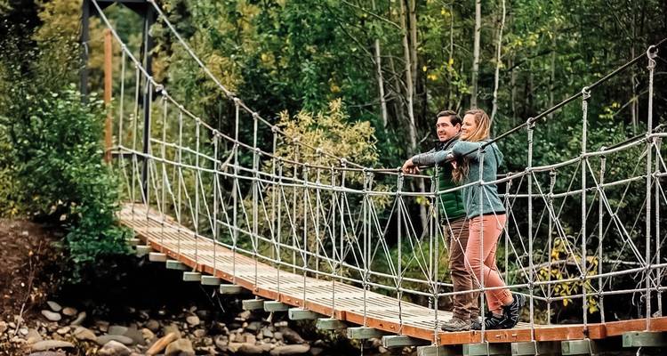 Paar steht auf einer Hängebrücke umgeben von Grün.