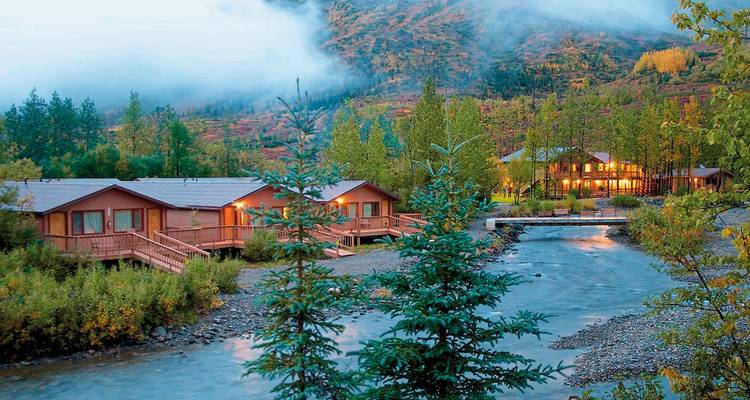 Hütte an einem Bach mit Bergen im Hintergrund.