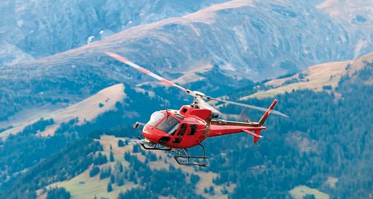 Rode helikopter die over bergachtig terrein vliegt.