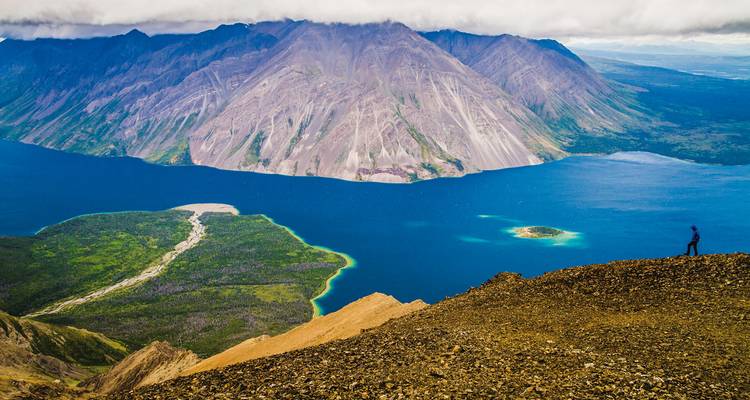 Personne faisant de la randonnée sur une crête montagneuse surplombant un magnifique lac bleu dans le parc national de Kluane.