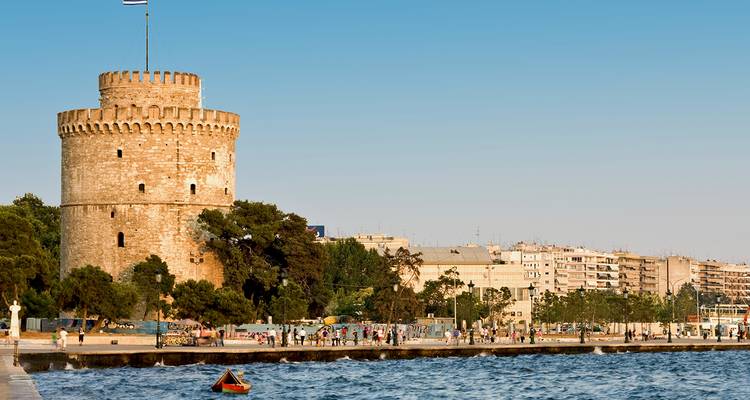 La histórica Torre Blanca de Tesalónica se alza en el paseo marítimo con mar en calma y luz dorada del atardecer.