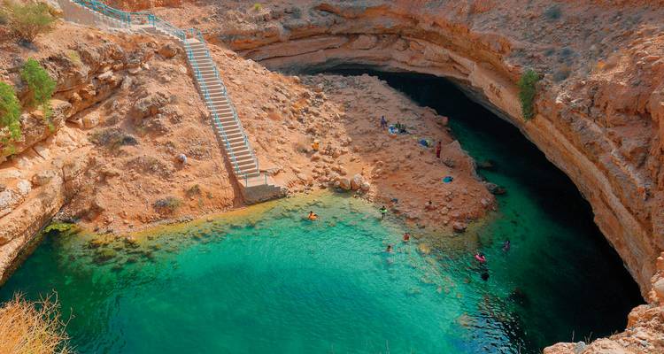 Sinkhole with turquoise water and people swimming.