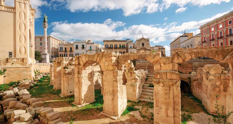 Ancient Roman ruins set in a city plaza under a bright blue sky.