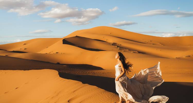 Frau in fließendem Kleid, die durch Sanddünen wandelt.