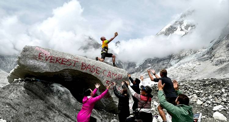 Gruppe von Menschen, die enthusiastisch in der Nähe eines Felsens posieren, der mit 'Everest Base Camp' beschriftet ist.