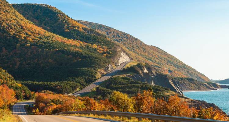 Carretera escénica Cabot Trail serpentueando entre colinas de colores otoñales sobre el océano en Cape Bretón