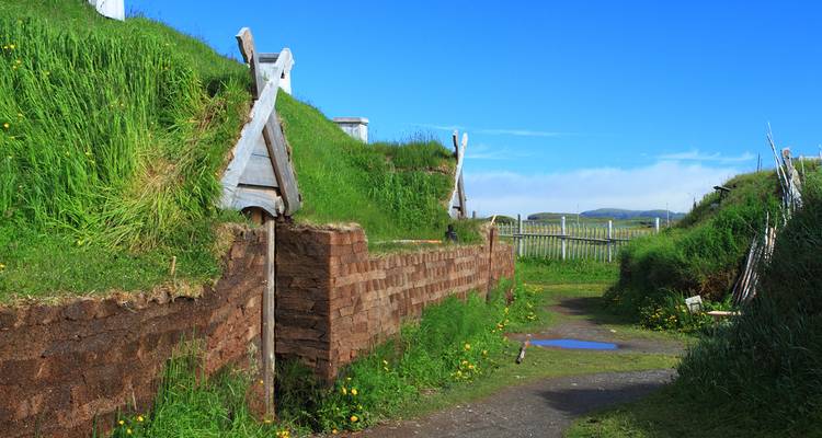 A reconstructed Viking village with sod-covered buildings and wooden structures under a bright blue sky.
