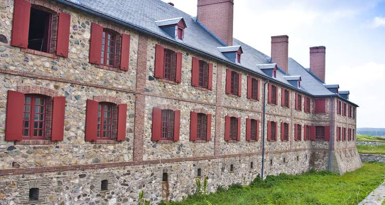 A historic stone building with red shutters under a cloudy sky.