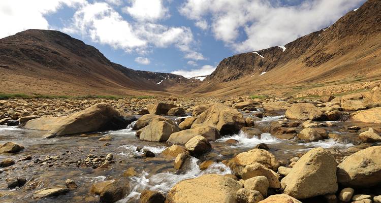 A scenic view of a rocky mountain landscape with a flowing stream under a partly cloudy sky.