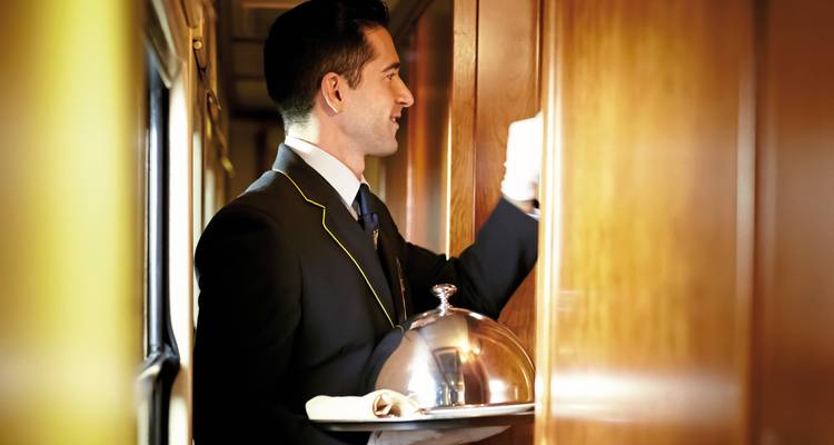 Treinbegeleider die een dienblad vasthoudt in een luxueus treincoupé