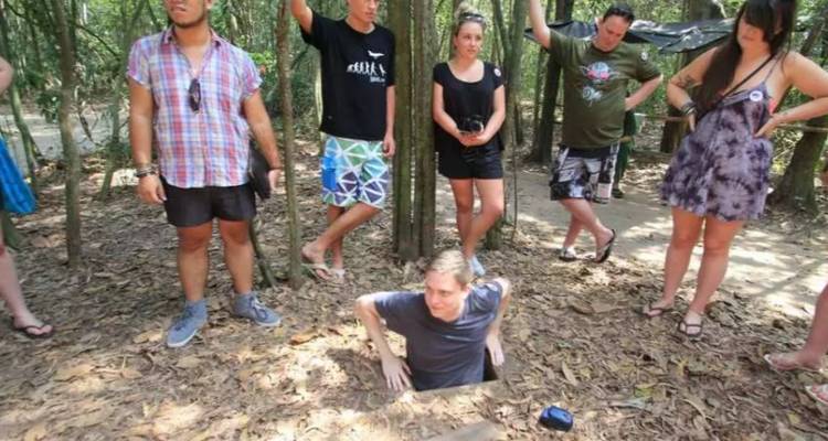 Des touristes observant une personne qui sort de l'entrée d'un tunnel dans la forêt.