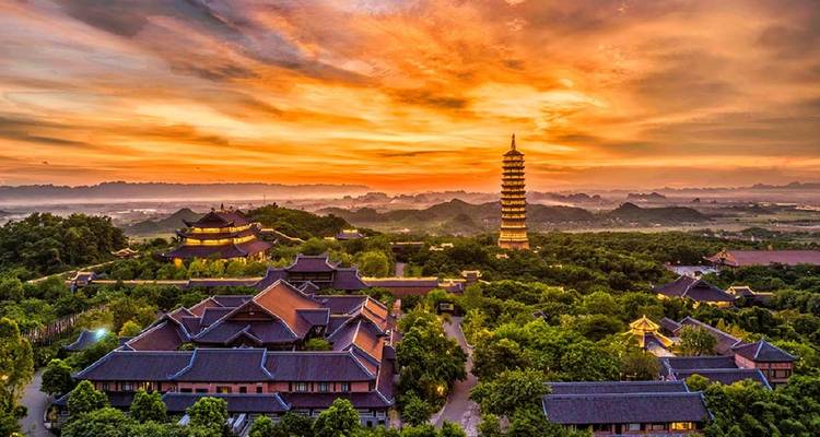 Pagode de Bai Dinh entourée d'une végétation luxuriante sous un coucher de soleil coloré.