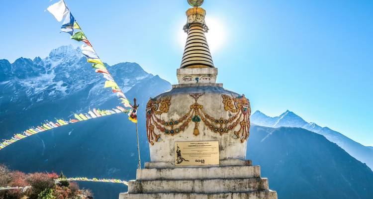 Stupa with colorful flags and a sunlit mountain view.