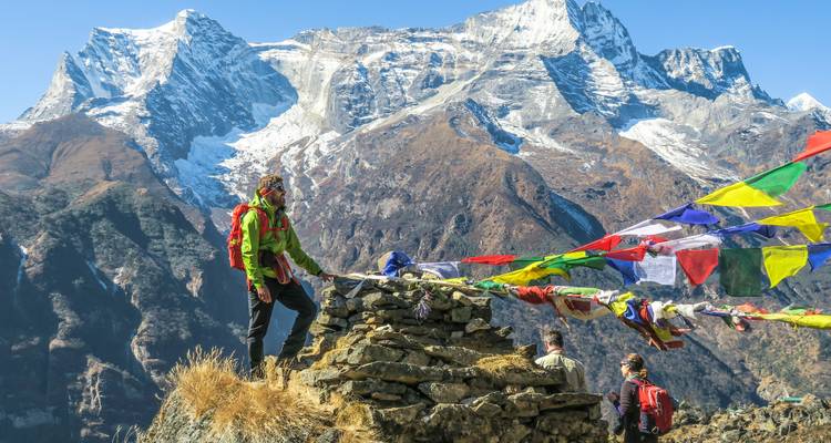 Hiker with prayer flags in front of a majestic mountain range.