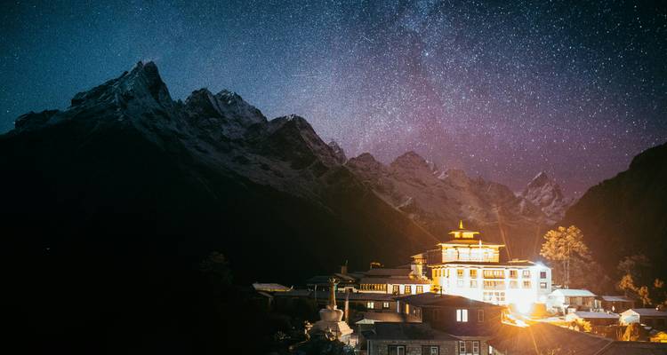 Verlicht gebouw met majestueus berglandschap onder sterrenhemel.
