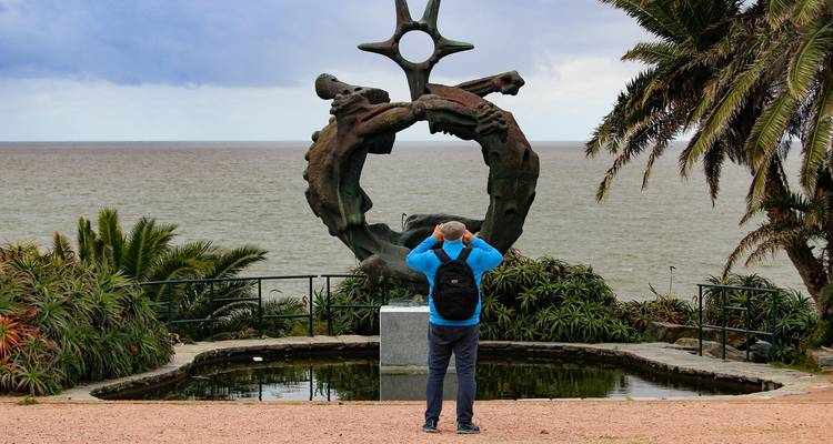 Person fotografiert eine Küstenskulptur mit Meerblick.