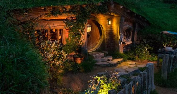 Cozy hobbit house with a round door at dusk.