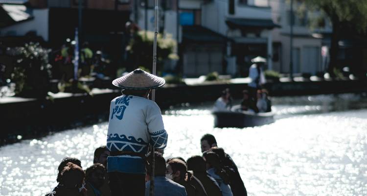 Eine Person, die ein traditionelles Boot auf einem Fluss rudert mit unscharfem Hintergrund.